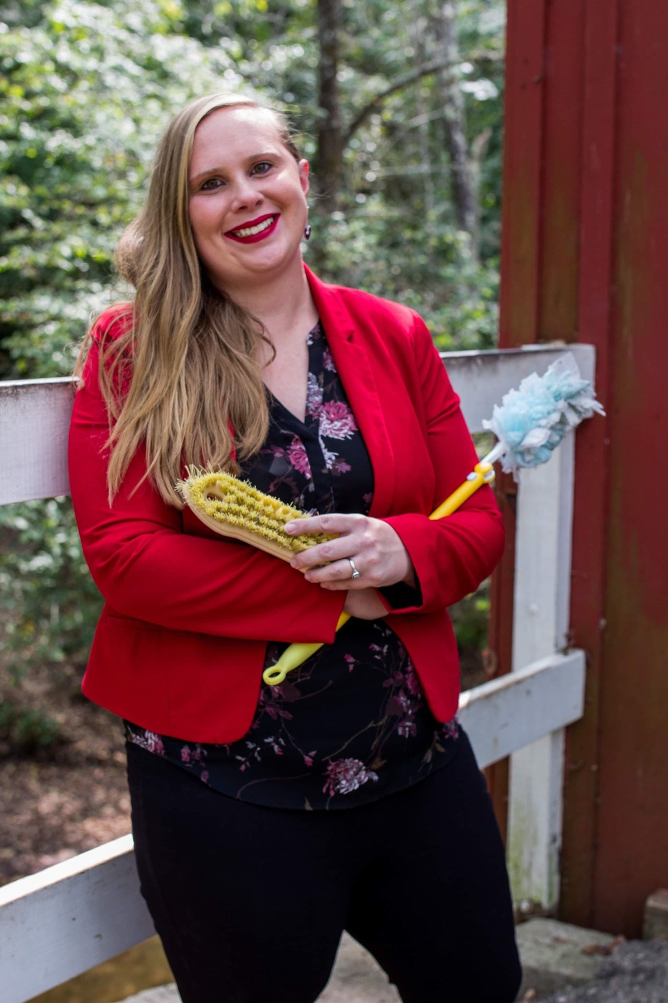 Liz Wiley with her arms crossed holding a bristle brush and a toilet brush.